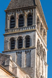 Saint-Philibert de Tournus.<br> Le grand clocher de la croisée, plus large que celui de la façade, domine le chœur et le transept de l’église. Elle fut commencée vers 1120 et ses trois étages furent édifiés en plusieurs étapes au 12e siècle. Le premier étage est décoré de bandes lombardes sur des modillons. Les deux étages supérieurs présentent des baies triples sur colonnettes, dont le premier possède des chapiteaux sculptés de masques étranges et de diables. L’étage supérieur conserve des pierres de bichromie rouge-blanc et un décor sculpté abondant rappelant Cluny III : colonnettes, pilastres cannelés, frises à motifs antiquisants, archivoltes lobées et modillons.