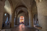 Saint-Philibert de Tournus. Le narthex <br>  Cette Galilée ou avant-nef des années 1030-1040 s’élève sur deux étages. La salle basse, trapue et obscure, fait office de vestibule de l’église. Elle comprend trois vaisseaux de trois travées reposant sur quatre énormes piles rondes maçonnées avec des impostes à double ressaut. Les voûtes du vaisseau central sont de larges arêtes sur doubleaux, celles des collatéraux sont en berceau transversal de la même hauteur. Les murs latéraux sont allégés de demi-colonnes. L’architecture et les voûtes reprennent alors l’exemple du 4e siècle de la Basilique de Maxence à Rome. Sept portes s’ouvrent dans les parois, dont trois sur la nef et deux autres ont été murées. Le sol du narthex, dont un rehaussement au 18e siècle rendant l’édifice plus bas, comprend des dalles funéraires du Moyen Age.  Ses piliers massifs soutiennent le poids de la chapelle Saint-Michel située au-dessus.