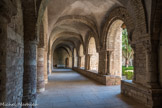 Saint-Philibert de Tournus. Le Cloître Saint-Ardain.<br> Le cloître de l’abbaye, au flanc sud de la nef de l’abbatiale, était au centre de l’abbaye. Du cloître construit par l’abbé Ardain vers 1030 ne reste qu’une seule galerie romane, accolée à l’église. En partie reconstruite aux 13e et 15e siècles et utilisée comme chapelle au 19e siècle, elle fut restaurée en 1957. Cette galerie nord présente six travées voûtées d’arêtes sur doubleaux. Quatre grandes arcades à double rouleau en plein cintre, portées par des colonnes engagées à chapiteaux, s’ouvrent sur le préau du cloître où se trouve un puits du 18e siècle. A l’intérieur de la galerie, le mur nord est décoré d’une longue série d’arcades aveugles sur demi-colonnes. L’architecture ressemble alors à celle du narthex, sensiblement de la même époque.