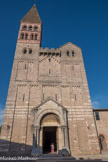 Saint-Philibert de Tournus.<br> Austère comme une forteresse, cette haute façade est un chef-d’œuvre de l’art lombard du début du 11e siècle. Construite en petits moellons, elle est décorée sur deux étages de plusieurs séries d’arcatures lombardes reliant des bandes en saillie. Les arcatures entourent d’étroites ouvertures qui se présentent comme des meurtrières éclairant le narthex et son étage. Au centre les arcatures s’élèvent en forme de triangle autour d’une ouverture en croix. Dans la partie haute de la façade on admire des frises de pierres en dents de scie et d’engrenage. Deux clochers, également du 11e siècle, s’élèvent au-dessus de la façade, présentant un étage avec des baies à colonnes et chapiteaux. Le clocher à droite se termine en bâtière, celui à gauche a été rehaussé par un campanile au 12e siècle. La tribune crénelée en haut de la façade et le portail central datent de la restauration de Questel au milieu du 19e siècle.