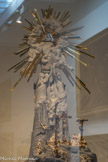 Via Vitae. <br> La Crucifixion et La Résurrection. Au sommet, l’Eucharistie présentée par deux allégories féminines : l’Amour, dont l’attribut est un sceptre surmonté de deux cœurs, et l’Harmonie dans l’attribut est une harpe. L’hostie sertie de diamants fait transparaître en rubis le monogramme du Christ et JHS (Jésus Sauveur des hommes). En partie sommitale, les rayons de la gloire divine entourent le triangle, Trinité de Dieu, en cristal de Roche.