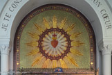 Au cœur du sanctuaire, la chapelle des Apparitions (XVIIe-XIXe siècles) <br> Au-dessus de la châsse,  la mosaïque représente le Cœur de Jésus  avec des flammes qui en jaillissent. Les flammes symbolisent l’amour ardent. La Croix est plantée dans le Cœur, et Celui-ci est entouré d’une couronne d’épines
