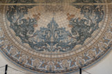 La ROSACE de la Société Anonyme des Carrelages Céramiques de Paray-le-Monial classée « Hors Concours » à l’Exposition Universelle de Paris en 1900
Historique et description d’un Chef d’Œuvre
« Cette rosace fut créée pour l’Exposition Universelle de Paris en 1900 par Paul Chamoz lui-même, dont la signature figure sur les plans destinés à la fabrication ainsi que sur un dessin préparatoire du palier qui ornait l’entrée du Palais de la Céramique de cette exposition et qui reprend un motif similaire mais selon un plan en arc outrepassé.
Elle se compose en son centre de quatre carreaux formant un cercle autour duquel prennent place concentriquement 34 rangées de carreaux trapézoïdaux où se déploient des motifs d’inspiration essentiellement végétale selon une symétrie centrale, dans des tons de camaïeux bleu turquoise ocre et gris sur fond clair.
L’observation montre que seule la partie centrale de la rosace est identique à celle exposée à l’intérieur de la galerie du Grand Palais (diamètre 9,50 m).
La rosace a été élargie vers l’extérieur (diamètre total 12,50 m) par l’adjonction d’un bandeau de carreaux concentriques, avec l’ajout : « Carrelages Céramiques de Paray-le-Monial »
Bien que nous ne sachions pas si cet ajout était prévu à l’origine et malgré une unité de coloris, ces deux parties présentent des différences stylistiques ».