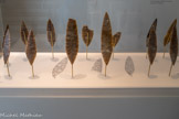 Ensemble des 13 pointes foliacées de la cachette de Volgu.
Environ -18 000 ans.
Les pointes de Volgu : un ensemble extraordinaire, par le choix maîtrisé de la matière première.
Le silex utilisé pour la fabrication des pointes de Volgu est de grain fin, homogène, sans défaut. Il doit se présenter sous forme de dalles d’au moins 30 cm de longueur.
Les différences de couleur visibles ont longtemps suggéré un approvisionnement aléatoire, effectué au gré des déplacements.
En réalité, un récent programme de recherches a révélé que le silex utilisé est extrait d’un seul secteur de la vallée de la Loire, à 150 km au nord-ouest de Volgu.
Par des proportions à la limite de la rupture
D’une taille comprise entre 23 et 37 cm pour une épaisseur n’excédant jamais 9 mm, elles reflètent une volonté de pousser l’art du façonnage lithique à la limite du point de rupture. Par l’excellence du geste L’observation minutieuse des pointes met en avant deux séries un peu différentes : une plutôt large, l'autre plus élancée.
Plusieurs hypothèses en découlent :
- cet ensemble aurait pu être réalisé par plusieurs artisans [au moins deux], identifiables grâce à ces légères différences techniques. / un seul artisan aurait également pu fabriquer ces pointes et les différences de traitement seraient alors le résultat d’une évolution de ses capacités techniques dans le temps.
- enfin, il se peut que le ou les artisans ai[en]t été obligé[s] de s’adapter aux aléas provoqués par la préparation des surfaces [fissures, fractures accidentelles de la forme d'origine etc].