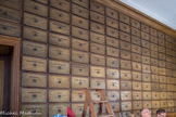 Le magasin. C'est la réserve de la pharmacie et le lieu de fabrication des médicaments. Dans cette pièce se trouvent 317 tiroirs en chêne, portant des inscriptions.
À stocker et conserver les matières premières nécessaires pour composer les remèdes.
Quelles informations donnent les inscriptions ?
Ce sont les noms des produits servant à fabriquer les médicaments.
On retrouve, rangés dans ces tiroirs, des éléments appartenant au monde :
végétal : environ 217 plantes sont identifiées (par exemple amandes douces, chicorée amère, mélisse, pimprenelle, digitale pourpre, cannelle ...) ;
animal : on compte 10 variétés (yeux d’écrevisse, cire jaune et blanche, corne de cerf, os de seiche, coraline, coquille d’huitre, mouche cantharide, cochenille, éponge) ;
minéral : Il ont été découverts dans les tiroirs (dont zinc, cuivre, fer, ocre jaune, plomb...).
On peut ainsi admirer la pharmacie du XVIIIe siècle abritant près de 400 tiroirs.