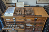 CASSE. Chaque casse est divisée en cassetins, qui permettent de classer toutes les lettres de l’alphabet en minuscules et en majuscules, ainsi que tous les chiffres, toute la ponctuation, toutes les lettres avec accent et les espaces de différentes largeurs. Ces caractères sont rangés de façon pratique : dans le bas de casse, les caractères les plus utilisés (les minuscules) et dans le haut de casse, les caractères les moins utilisés (les majuscules et les lettres avec accent). Le plus grand cassetin contient la lettre « e » car c’est la lettre la plus utilisée dans la langue française. Le typographe, après avoir posé sa casse sur un plan incliné (le « rang »), composait son texte dans un composteur. Le composteur est une réglette en acier que l’on ajuste à la largeur du travail à composer. Le typographe prenait un caractère dans la casse et le posait à l’envers dans le composteur (de la gauche vers la droite), puis il posait un deuxième caractère et ainsi de suite... Les espaces sont matérialisés par une barrette de plomb moins haute que les caractères. Jusqu’en 1918, tous les textes du journal étaient composés manuellement, caractère par caractère.