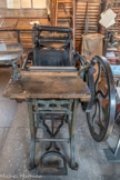 LA MINERVE BERTHIER.
C’est la presse la plus ancienne de l’atelier. Elle date de 1869. C’est une presse à platine. La forme se place à la verticale, contre le marbre (surface plane en acier).
On dépose de l’encre à l’aide d’une spatule sur la table d’encrage en forme de disque. On actionne les trois rouleaux de la presse qui remontent sur la table d’encrage, étalant alors l’encre. Avant d’imprimer, il faut encrer les caractères de la forme ; les trois rouleaux qui ont étalé l’encre sur la table d’encrage ont maintenant un autre rôle : ils vont aller se charger en encre en passant sur le disque puis ils vont la déposer sur les caractères en passant sur la forme.
La mise en place du papier : l’imprimeur prend une feuille puis la pose délicatement contre les 3 épingles métalliques (« crapaudines ») qui se trouvent sur l’habillage de la presse. L’encrage et l’impression sont actionnés par une pédale, ce qui libère les deux mains de l’imprimeur.