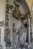 Cimetière monumental de Staglieno. <br> Sculpteur D. Carli, 1892. De ces vieux couples respectables, un beau groupe de la galerie frontale nous offre une illustration sur le thème des retrouvailles dans l’au-delà : statufiés en pied, sortant dirait-on chacun d’une porte, mari et femme se rencontrent cérémonieusement, l’épouse porteuse de son voile de veuve, une main sur le cœur, l’autre placée dans celle du mari, avec lequel elle semble échanger un bouquet de fleurs. L’attitude de l’homme est plus théâtrale, qui brandit de la main gauche un crucifix en guise de bienvenue : le thème des retrouvailles individuelles s’inscrit ici sans heurt dans une atmosphère de religiosité traditionnelle.