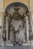 Cimetière monumental de Staglieno. <br> Sculpteur D. Carli, 1892. De ces vieux couples respectables, un beau groupe de la galerie frontale nous offre une illustration sur le thème des retrouvailles dans l’au-delà : statufiés en pied, sortant dirait-on chacun d’une porte, mari et femme se rencontrent cérémonieusement, l’épouse porteuse de son voile de veuve, une main sur le cœur, l’autre placée dans celle du mari, avec lequel elle semble échanger un bouquet de fleurs. L’attitude de l’homme est plus théâtrale, qui brandit de la main gauche un crucifix en guise de bienvenue : le thème des retrouvailles individuelles s’inscrit ici sans heurt dans une atmosphère de religiosité traditionnelle.