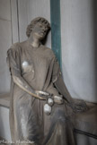 Cimetière monumental de Staglieno. <br> Tombe Erba, 1883, sculpteur Santo Saccomanno. La tombe de Carlo Erba, commerçant et politicien affirmé, a été commandée par un parent. Ce monument présente les formes d’une cathédrale néogothique ; à l’intérieur, sur le sarcophage, estnassise une femme avec des graines de pavot, un symbole païen de l’oubli éternel, entre les doigts de sa main droite, abandonnée sur son giron. Sa veste qui glisse le long de son bras découvre son épaule, lui conférant ainsi un brin de sensualité insolite pour l’époque, qui a donné lieu à beaucoup de polémiques. Cette personnification du Sommeil Éternel transpose l’image de la mort dans une dimension pré-symboliste, voire laïque, malgré la présence d’une grande croix au fond, et elle met en évidence sa partie liée au mystère et au vide.