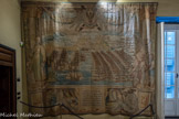 Villa del Principe. Palais d'Andrea Doria.<br> Salle du Naufrage. La dernière tapisserie de la série décrit le retour de la flotte victorieuse à Corfou, dont la silhouette se détache sur le fond. Les galères chrétiennes trament les navires turcs faits prisonniers par le truchement des cordages de remorques. Au premier plan on peut voir la Capitana nova de Giovanni Andrea avec un précieux butin de guerre: le navire amiral turc. Chez les collections Doria on a récemment trouvé un drapeau avec des emblèmes ottomans qui pourrait faire partie du butin ramené en Italie par l’amiral. Enfin, en ce qui concerne l’iconographie, on peut voir à gauche la Gloire, caractérisée par le cygne sur le piédestal et à droite la Renommée, avec la trompette, la foudre, la lance et les ailes incrustées d’yeux, oreilles et langue