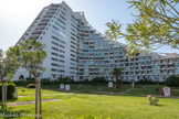 La Grande-Motte. <br> La grande pyramide est le bâtiment emblème de La Grande Motte. Avec ses 15 étages, c'est la construction la plus haute de la ville. Elle est dessinée par Jean Balladur qui lui donne la fonction de bâtiment de transition, de césure, entre les deux principaux quartiers de La Grande Motte : d'un côté, le Centre-Ville, avec ses pyramides tronquées, de l'autre, le Couchant, avec ses bâtiments aux formes ondulantes. La grande pyramide est la synthèse de ces formes à la fois masculines et féminines. Albert Marchais, sculpteur et peintre, réalise les médaillons qui ornent les jardins.