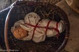 Bébé d'une paysanne, emmailloté avec un ruban rouge contre la rougeole.