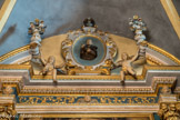 Saint-Sauveur-sur-Tinée <br> Retable du Rosaire. Les chapiteaux composites portent une architrave très classique, ornée de rinceaux et de séraphins, sur laquelle se développe un fronton en arc de cercle interrompu portant deux vases à bouquet et habité d'angelots qui présentent, sous un vase plus petit, un médaillon avec la figure de saint Dominique vêtu de bure et tenant en mains le chapelet du Rosaire.
