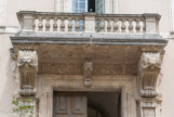 <center>Le palais de justice.</center>Le décor au centre : le balcon et la balustrade sont en pierre car nous sommes au XVIIe. Sous le balcon, des lions avec des draperies dans la gueule, au centre, un Mascaron.