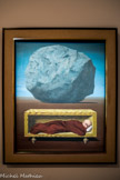 <center>René Magritte</center>Lessines (Belgique), 1898 - Schærbeek (Belgique), 1967.
Le Cap des tempêtes. 1964.
Huile sur toile. Cet étrange et inquiétant tableau montre un individu solitaire, dormant dans un meuble, à l’apparence d'un cercueil. Au-dessus de cet homme un rocher ou un météorite apparaît en songe. Il rappelle que le dormeur est vulnérable aux dangers de la nuit. les deux ombres n'ont pas la même direction. Chez Magritte la peinture n’est pas une fin en soi mais un véhicule pour atteindre « les mystères du monde ». Sa peinture est une pensée qui transgresse notre accoutumance au réel, combat la paresse de l’esprit : « L’art, tel que je le conçois, est réfractaire à la psychanalyse : il évoque le mystère sans lequel le monde n’existerait pas [...] Pour peindre le Mystère du monde je dois être bien éveillé, ce qui signifie cesser de m'identifier entièrement à des idées, des sentiments, des sensations. Le rêve et la folie sont au contraire propices à une identification absolue »