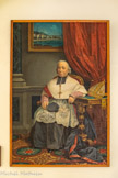 <center>Jour 3. Le couvent de Saint-François à Vico.</center>Monseigneur Xavier Toussaint Raphaël Casanelli d’Istria.Huile sur toile, cadre rapporté, 1865. Ce portrait de Mgr Casanelli d’Istria, évêque d’Ajaccio du 8 décembre 1833 au 12 octobre 1869, a été exécuté en 1865 par le peintre italien Matteo Marcellino. Le prélat est, ici, représenté sur un fond d’architecture, assis, de trois-quart, accoudé à un meuble d’appui au pied en bois doré, tourné, mouluré, chantourné, au décor en relief rapporté, orné sur sa face antérieure des armoiries épiscopales et de sa devise sur un phylactère ondé: « Auxilium de Sancto » (« Du sanctuaire qu’il t’envoie le secours », cf Psaume de David 20), inscrites dans un cartouche octogonal.
Il est revêtu de la soutane prélatice à la traîne déployée, portée sous un rochet en dentelle avec une mozette par-dessus, un rabat noir bordé de blanc cachant l’échancrure du col de la soutane.
La barrette à houppe posée sur ses genoux, l’anneau pastoral serti d’une améthyste, à l’annulaire de la main droite, la croix pectorale, la mitre précieuse rehaussée de broderies et de pierreries complètent sa tenue d’évêque.
Barrant le fond de la composition, une tenture pourpre, drapée sur le côté, laisse entrevoir, accroché au mur, un tableau figurant sa cité épiscopale.